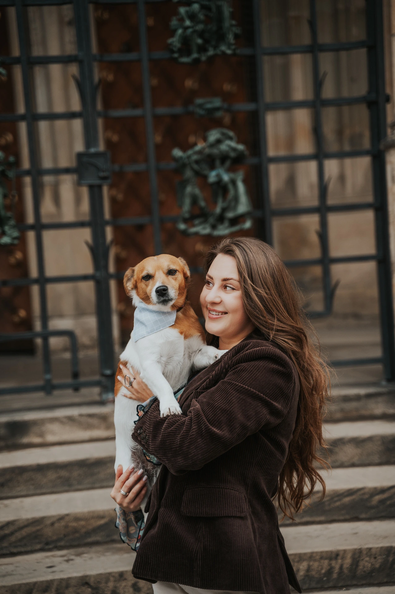 Woman holding her small dog Amigo in front of a decorated cathedral door during their Prague couple photoshoot.