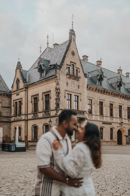 Prague couple photoshoot with castle architecture in focus Soft-focus couple kissing in the foreground with the castle courtyard architecture in focus during their Prague photoshoot.