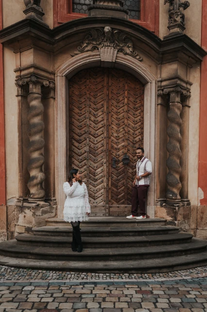 Couple smiling towards each other across the curved steps of a decorated wooden doorway during their Prague photoshoot.