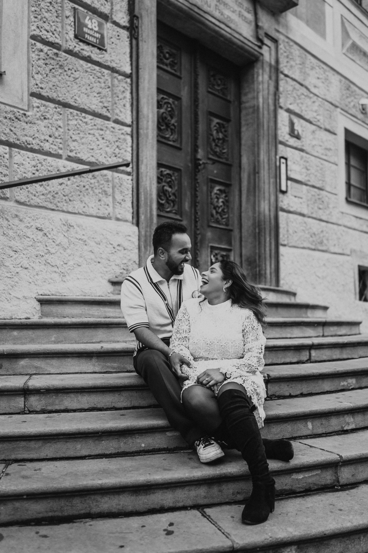 Black-and-white portrait of the couple sitting together on steps beside a castle doorway during their Prague photoshoot.