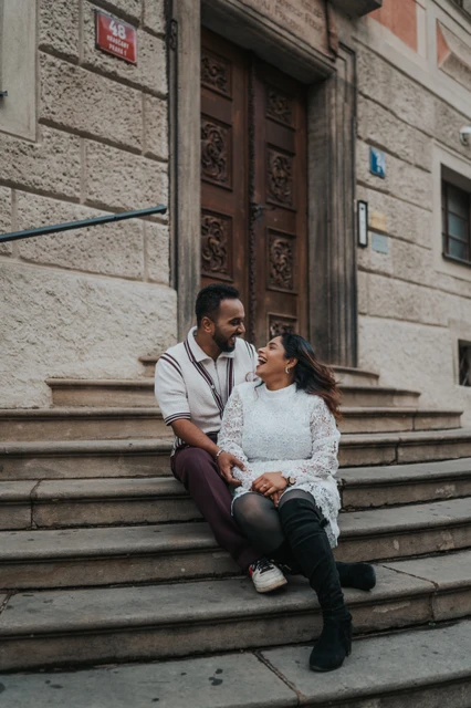 Couple smiling at each other while sitting on the stone steps at Prague Castle during their photoshoot.