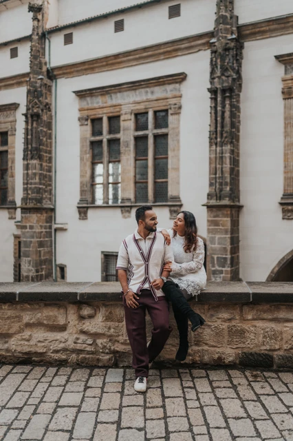 Prague couple photoshoot on a stone ledge at the castle Couple sitting together on a stone ledge beside the castle facade during their couple photoshoot in Prague.