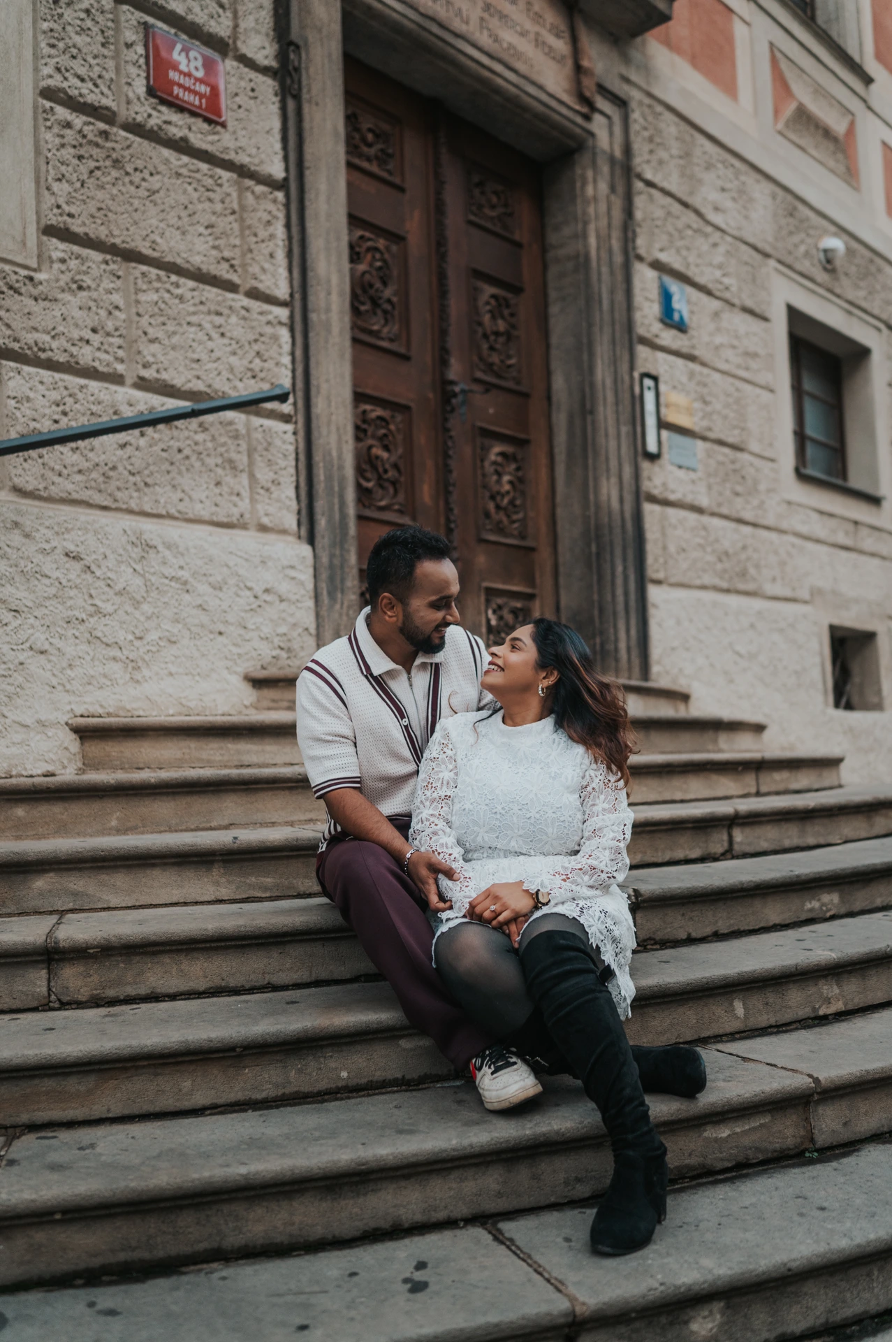 Couple sitting close together on stone steps beside a wooden doorway during their couple photoshoot at Prague Castle.