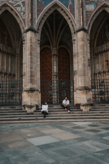 Prague couple photoshoot under the cathedral Gothic arches Wide vertical view of the couple seated apart beneath the pointed cathedral arches during their couple photoshoot at Prague Castle.