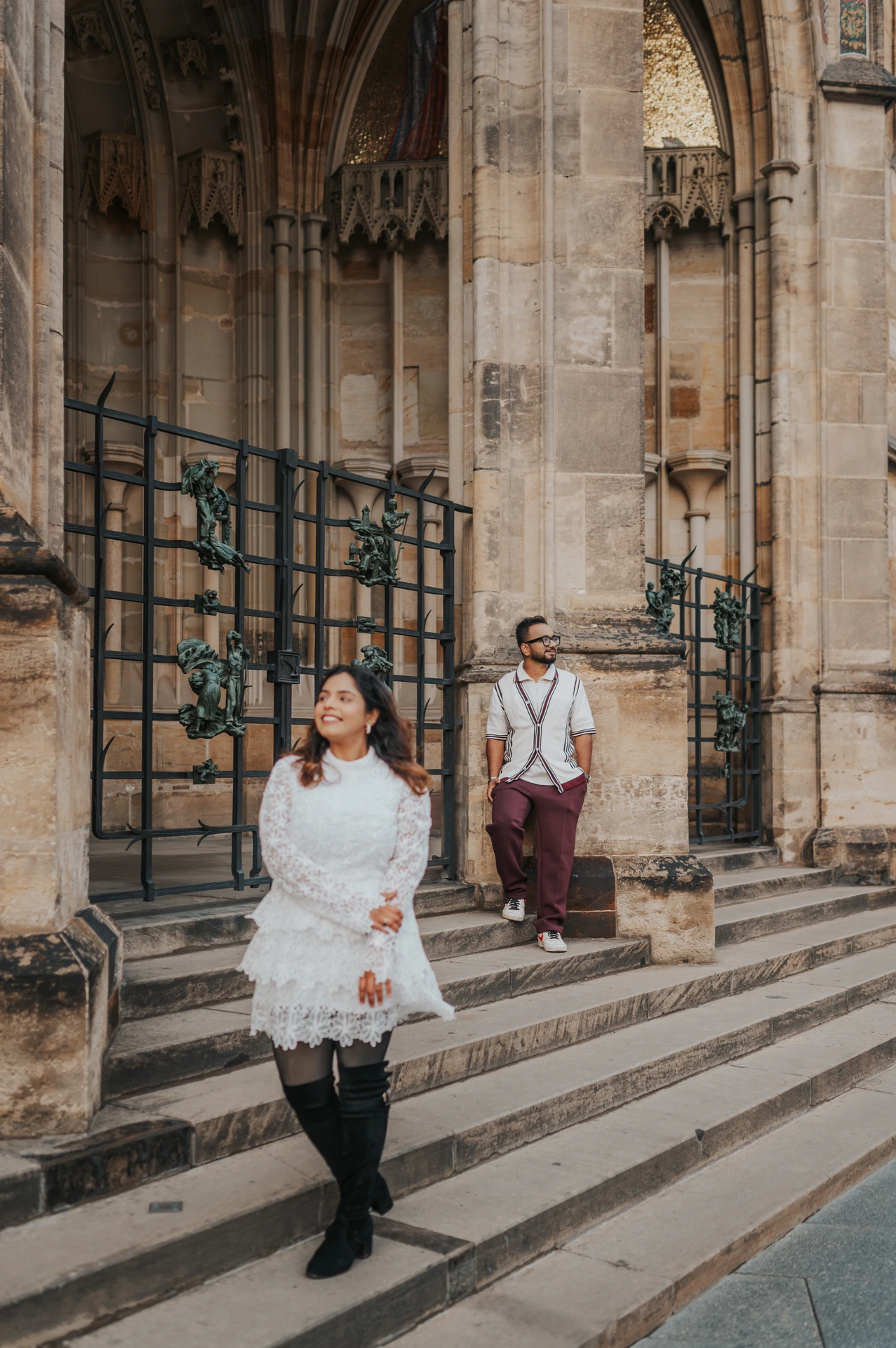 Woman walking down the St. Vitus Cathedral steps with her husband behind her during their couple photoshoot in Prague.