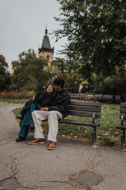 Prague couple photoshoot: an embrace on the park bench Couple embracing on a park bench beside fallen leaves and flowerbeds during their Prague couple photoshoot.