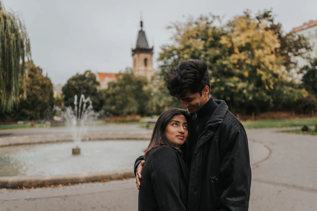 Prague couple photoshoot: a kiss beside the Charles Square fountain Wide close portrait of the man kissing his partner's head beside the Charles Square Park fountain during their Prague couple photoshoot.