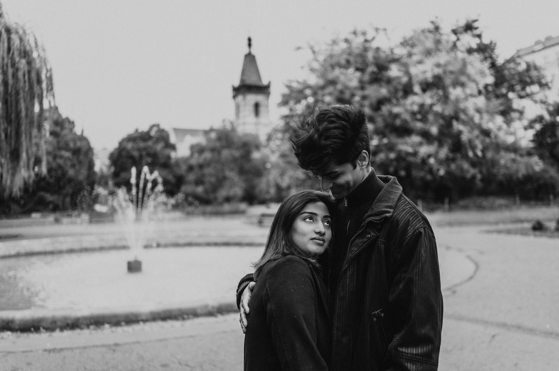 Black-and-white close portrait of the couple embracing beside the fountain with the New Town Hall tower behind them during their Prague couple photoshoot.