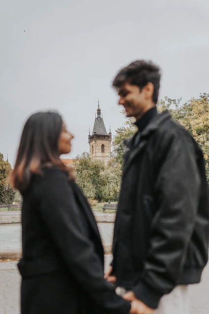 Prague couple photoshoot: a playful close-up in Charles Square Park Close portrait of the couple facing each other with the man smiling and the park softly blurred behind them during their Prague couple photoshoot.