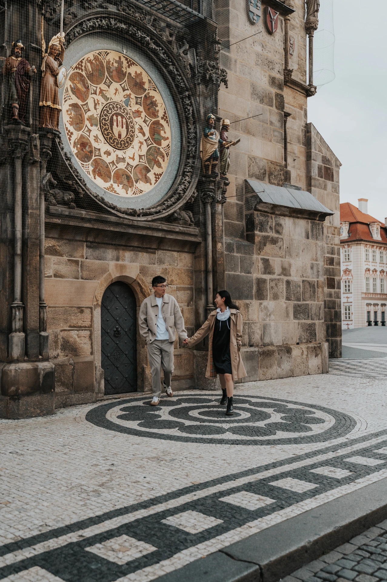 Couple walking in front of the Astronomical Clock across Old Town's patterned pavement during their Prague couple photoshoot.
