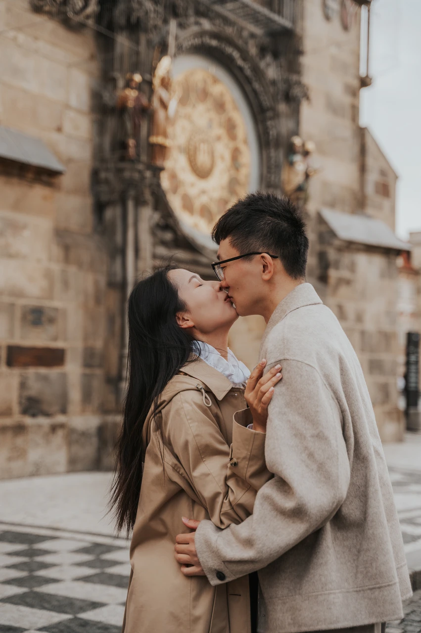 Couple photoshoot in Prague: a kiss with the Astronomical Clock behind them Close portrait of the couple kissing with the Astronomical Clock behind them during their Prague couple photoshoot.
