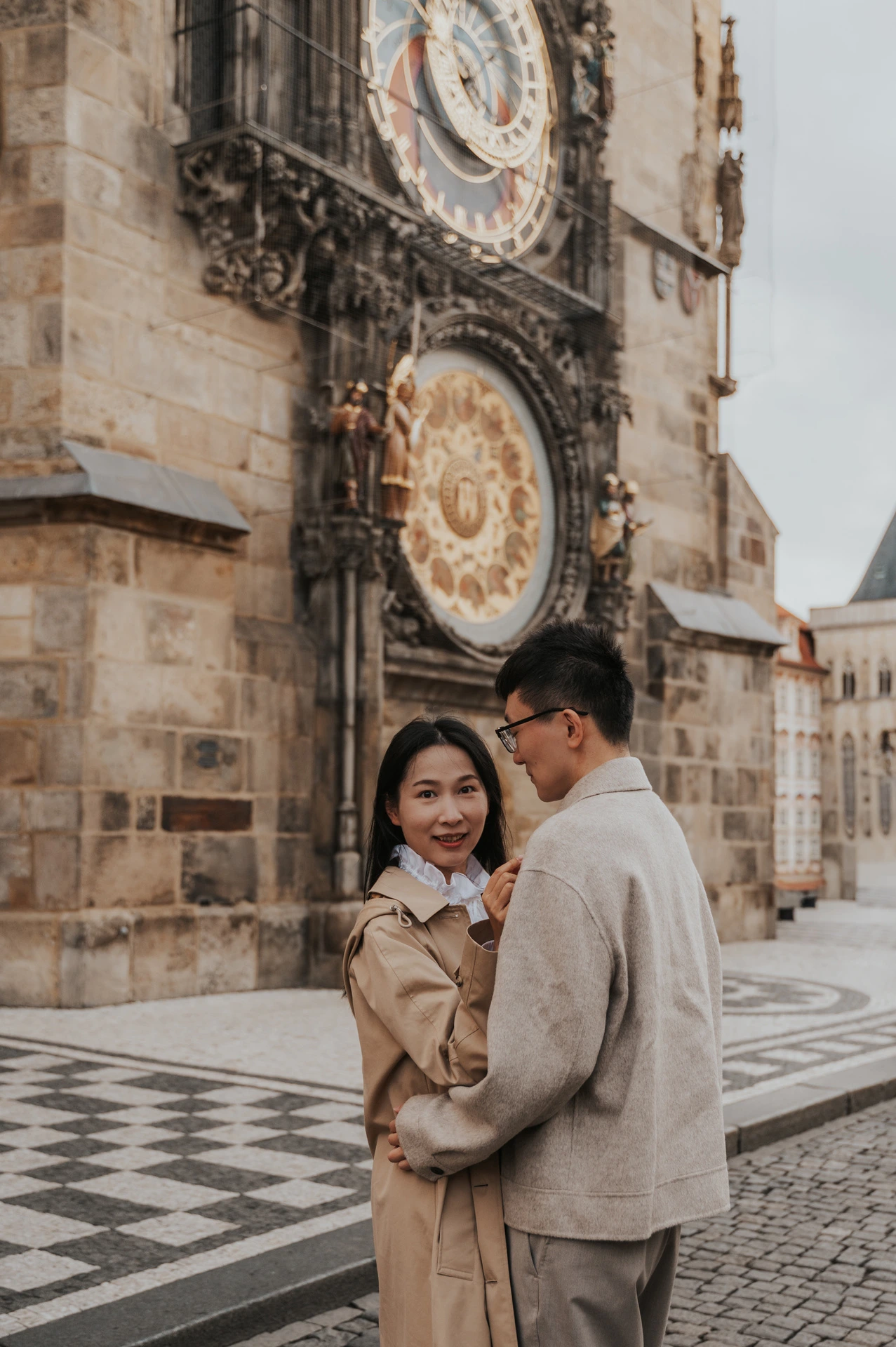Couple embracing in a wider portrait with the Astronomical Clock and patterned paving around them during their Prague couple photoshoot.