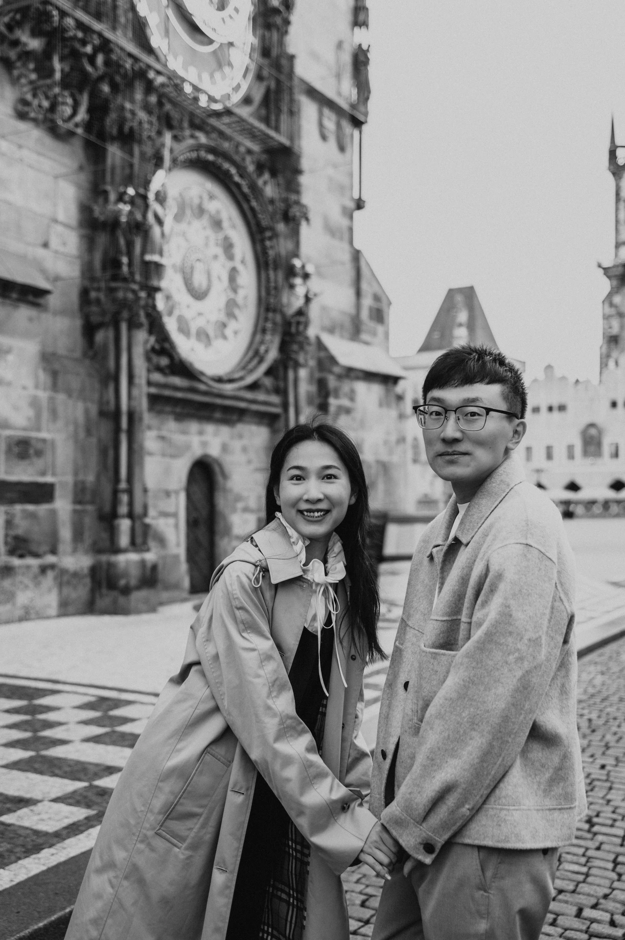 Black-and-white portrait of the couple holding hands beneath the Astronomical Clock during their Prague couple photoshoot.