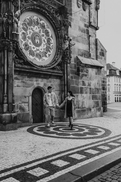 Couple photoshoot in Prague: a black-and-white walk by the Astronomical Clock Black-and-white photograph of the couple walking across the patterned pavement below the Astronomical Clock during their Prague couple photoshoot.