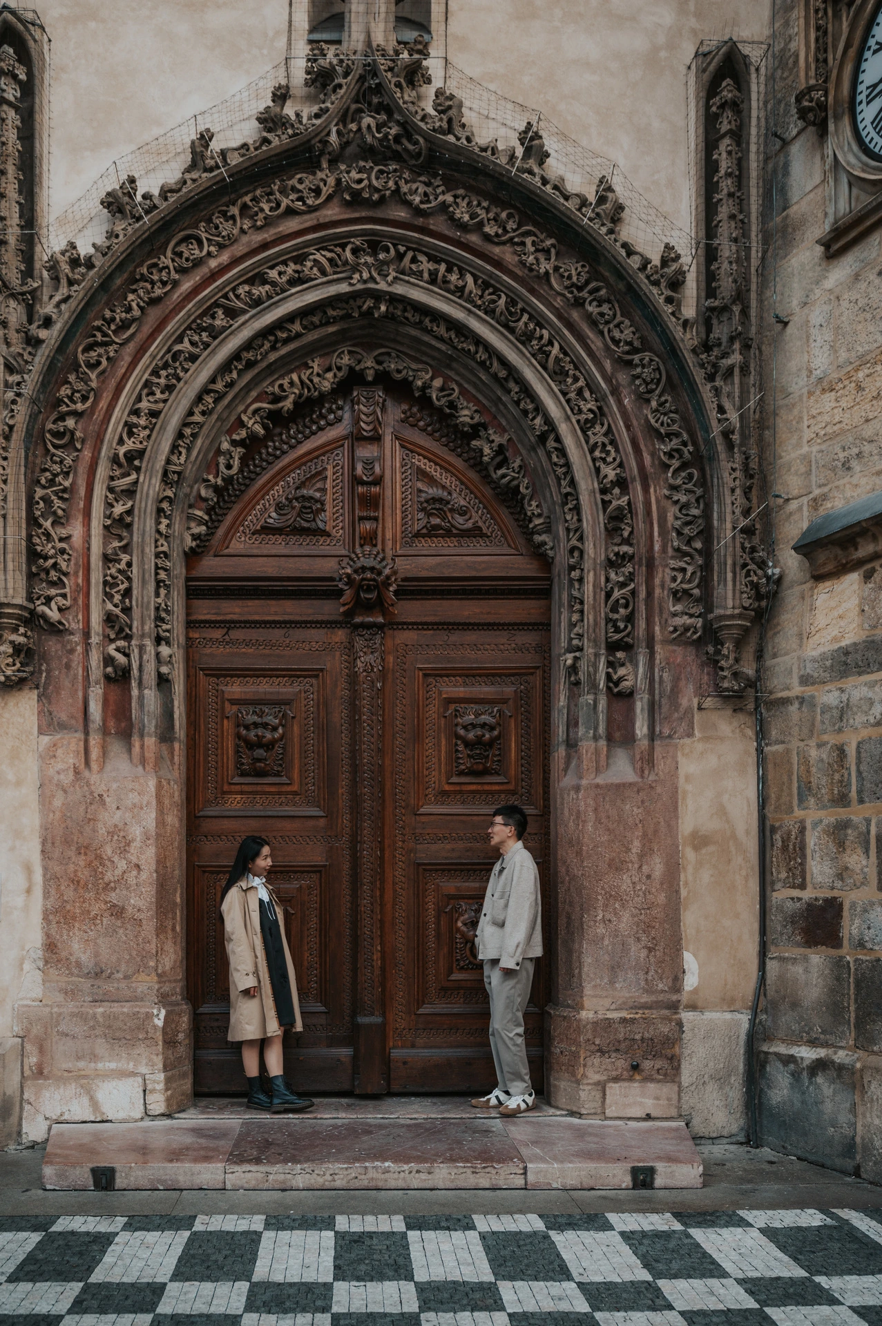 Couple standing on opposite sides of an ornate Gothic doorway at Prague's Old Town Hall during their Prague couple photoshoot.