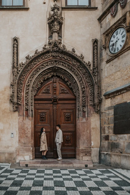 Couple photoshoot in Prague: an embrace beneath the Gothic doorway Couple embracing beneath the carved stone arch of the Old Town Hall's wooden doorway during their Prague couple photoshoot.