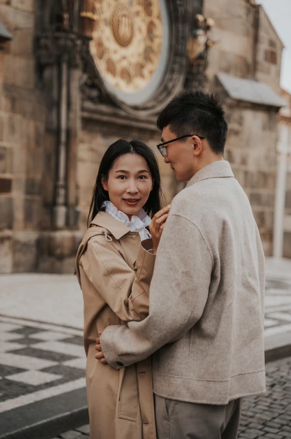 Couple photoshoot in Prague: a close embrace beside the Astronomical Clock Woman looking towards the camera as the couple embrace beside the Astronomical Clock during their Prague couple photoshoot.