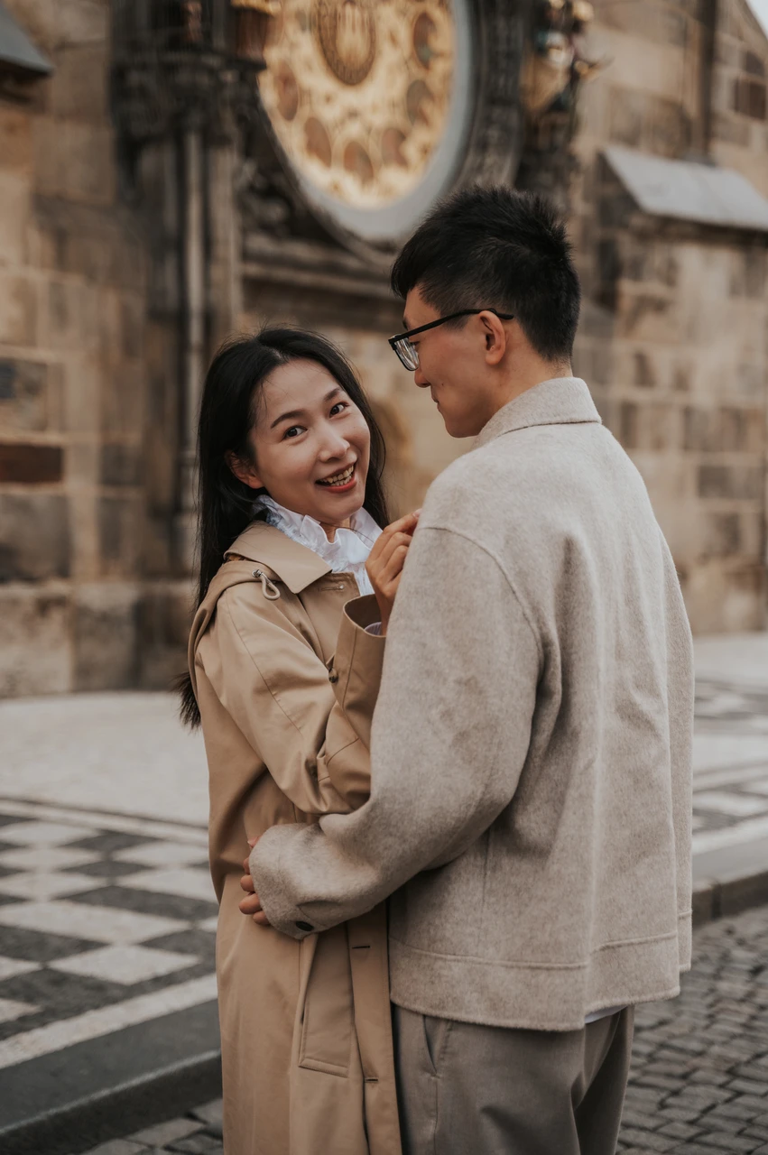 Couple photoshoot in Prague: smiling at each other in Old Town Woman smiling at her partner as they embrace near the Astronomical Clock during their Prague couple photoshoot.