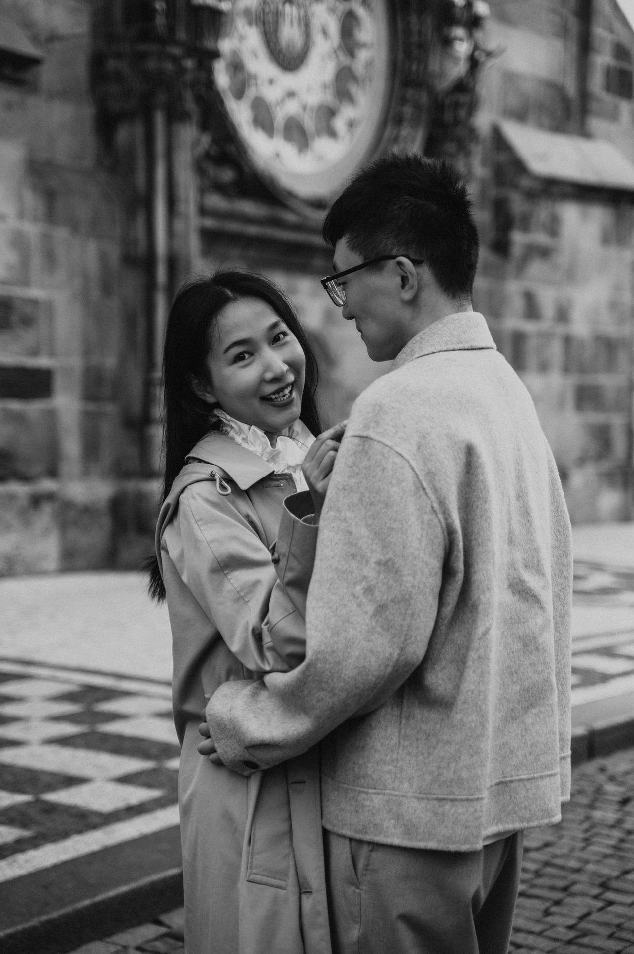 Black-and-white portrait of the couple smiling at each other beside the Astronomical Clock during their Prague couple photoshoot.