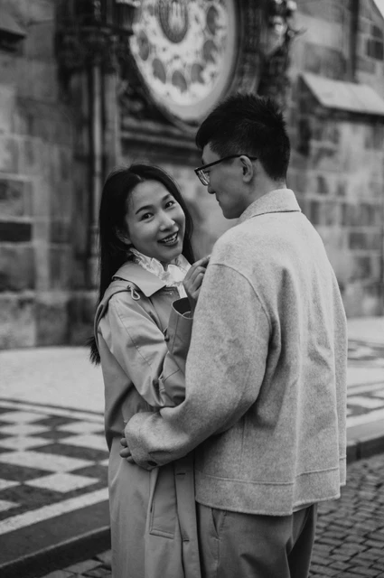 Couple photoshoot in Prague: a black-and-white embrace in Old Town Square Black-and-white portrait of the couple smiling at each other beside the Astronomical Clock during their Prague couple photoshoot.