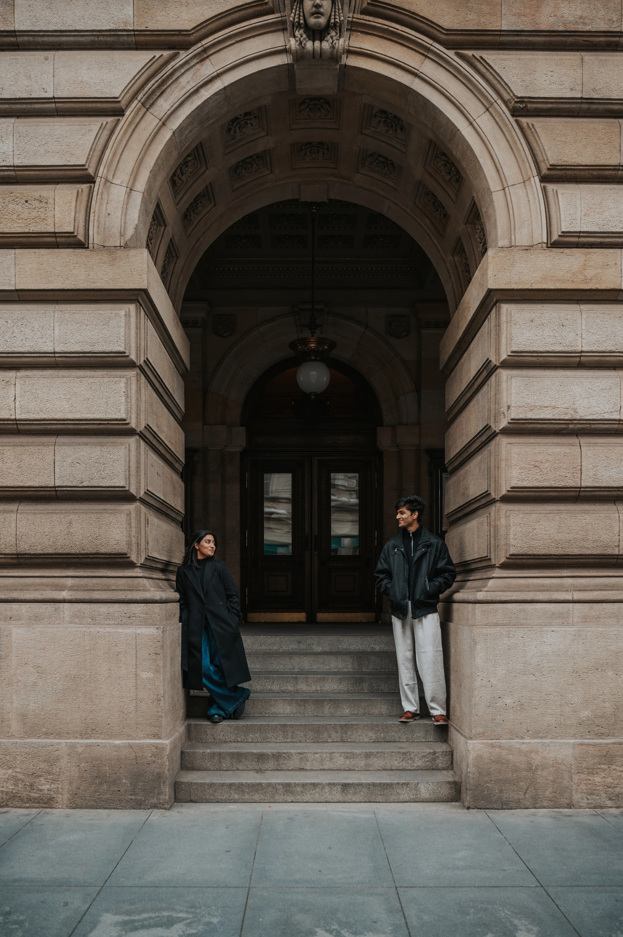 Couple facing each other from the stone sides of an arched theatre entrance during their Prague couple photoshoot.