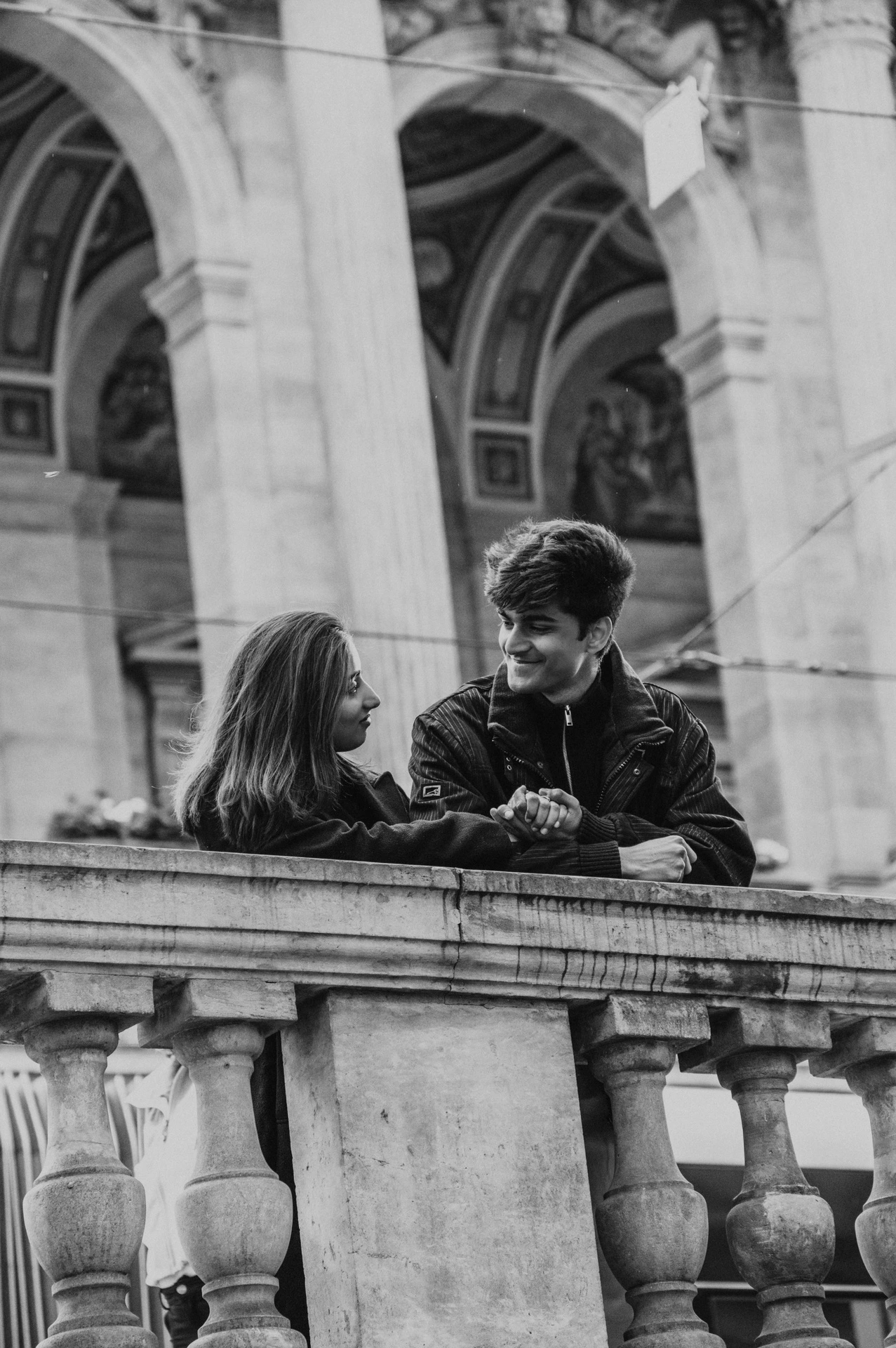 Black-and-white portrait of the couple smiling across a stone theatre balustrade during their Prague couple photoshoot.