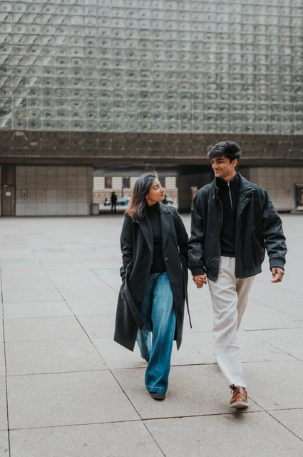 Prague couple photoshoot: a casual walk beside the modern theatre facade Couple walking hand in hand in jeans beside a textured modern facade during their Prague couple photoshoot.