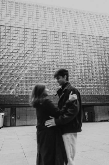 Prague couple photoshoot: a black-and-white embrace by the theatre Black-and-white portrait of the couple embracing in front of a textured modern facade during their Prague couple photoshoot.