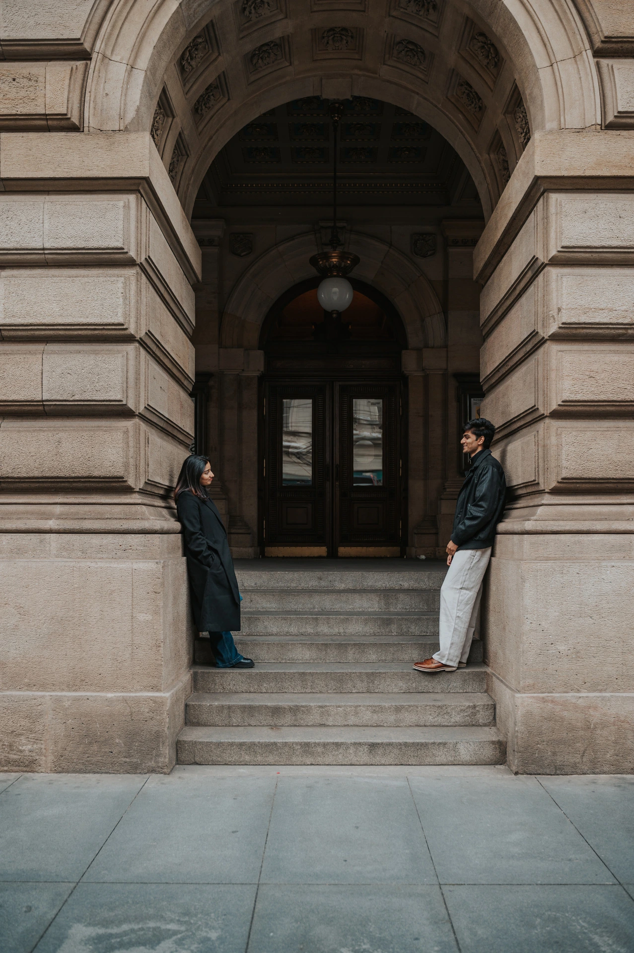 Couple standing on opposite sides of a tall arched entrance at the National Theatre during their Prague couple photoshoot.