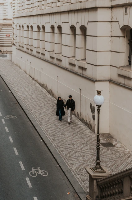 Overhead view of the couple walking beside the theatre's long stone wall and a street lamp during their Prague couple photoshoot.