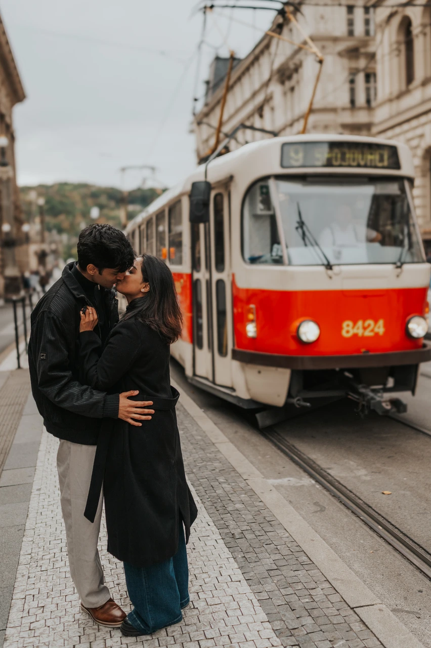 Prague couple photoshoot: a close kiss beside a red Prague tram Couple kissing beside a red and cream tram on a Prague street during their Prague couple photoshoot.