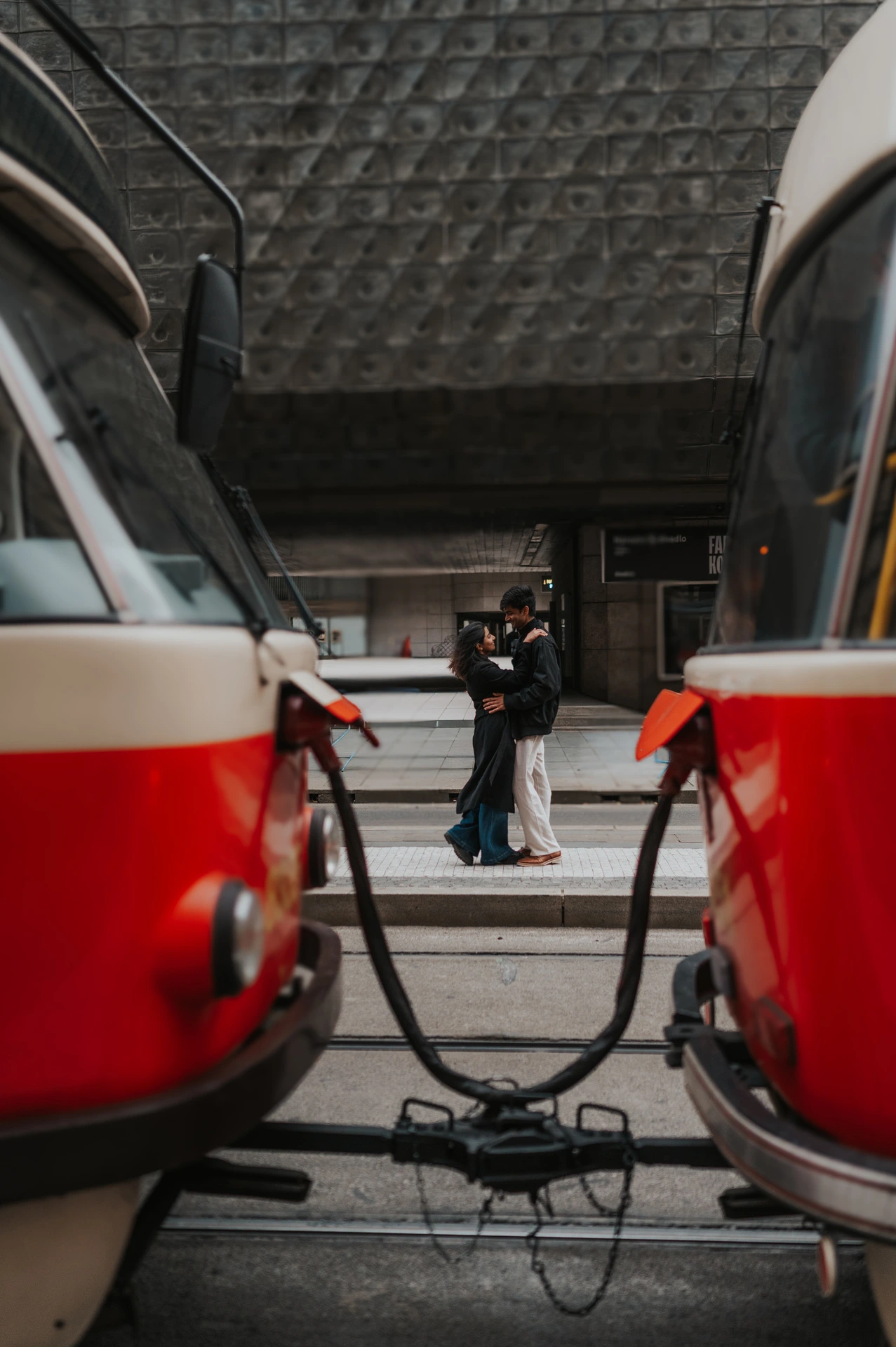 Prague couple photoshoot: an embrace framed by red trams Couple embracing on the theatre steps framed between two red and cream Prague trams during their Prague couple photoshoot.