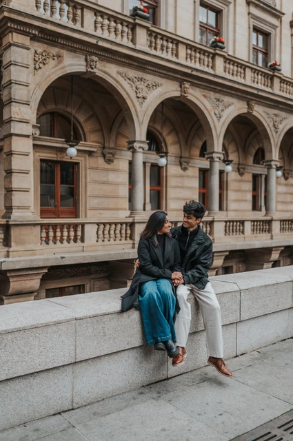 Prague couple photoshoot: sitting together beneath the theatre arches Couple sitting close on a stone ledge with the National Theatre arches behind them during their Prague couple photoshoot.