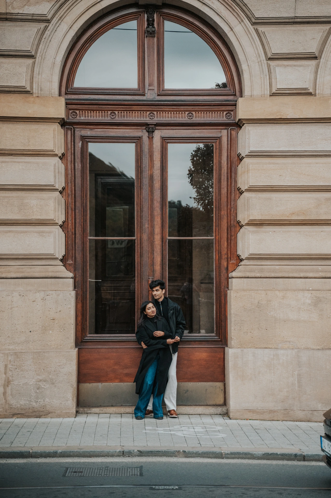 Couple embracing beneath a tall arched window on the National Theatre facade during their Prague couple photoshoot.