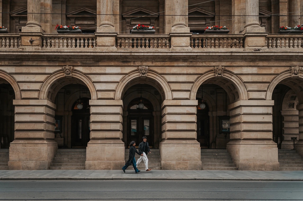 Prague couple photoshoot: hand in hand against the grand theatre facade Couple holding hands beneath an arch in a wide view of the historic theatre facade during their Prague couple photoshoot.