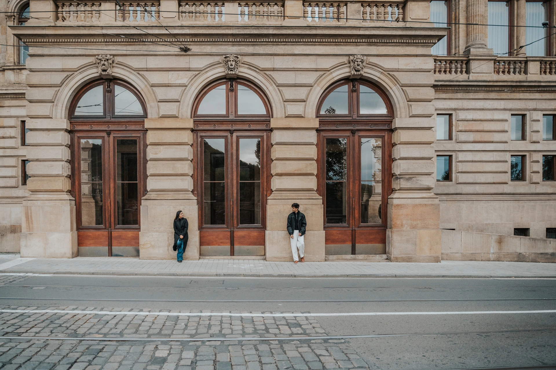 Prague couple photoshoot: a wide portrait beside the theatre doorway Wide view of the couple facing each other on opposite sides of a large wooden theatre doorway during their Prague couple photoshoot.