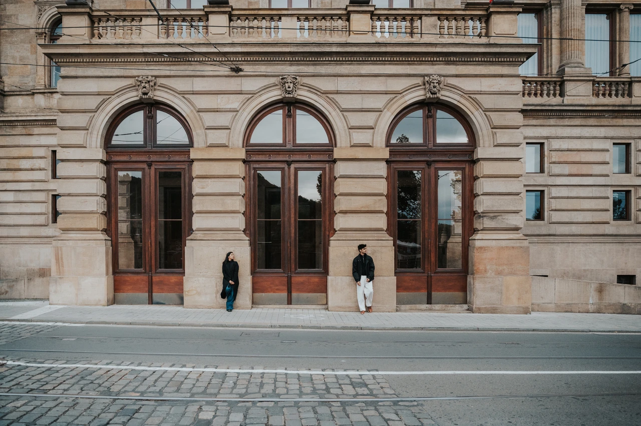 Prague couple photoshoot: a doorway portrait with room for the architecture Wide photograph of the couple standing apart beneath an arched wooden doorway at the theatre during their Prague couple photoshoot.