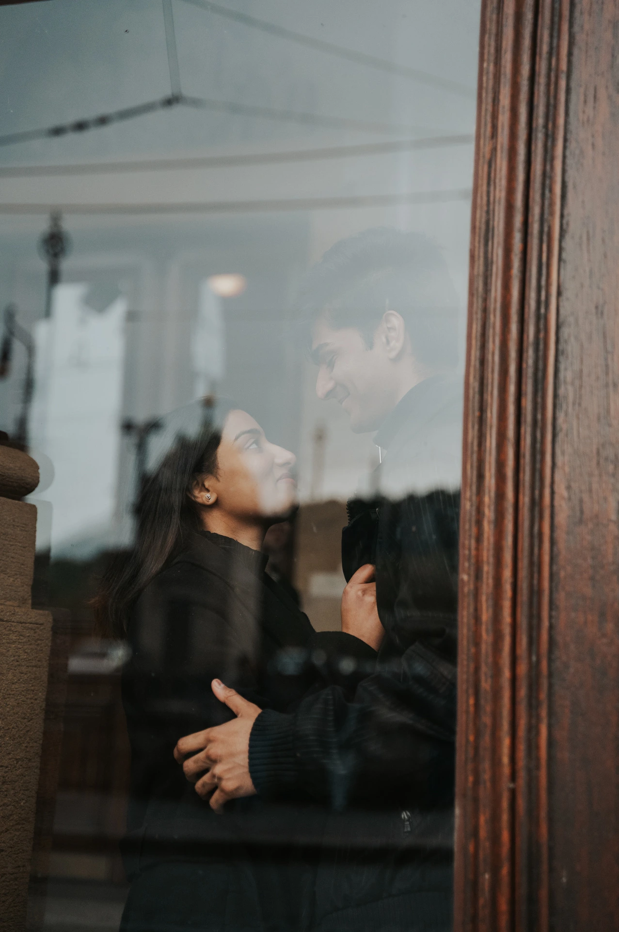 Close portrait of the couple looking at each other behind a reflective theatre window during their Prague couple photoshoot.