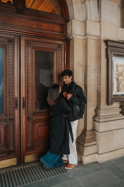 Prague couple photoshoot: a kiss beside the wooden theatre door Couple sharing an affectionate moment beside a tall wooden theatre door during their Prague couple photoshoot.