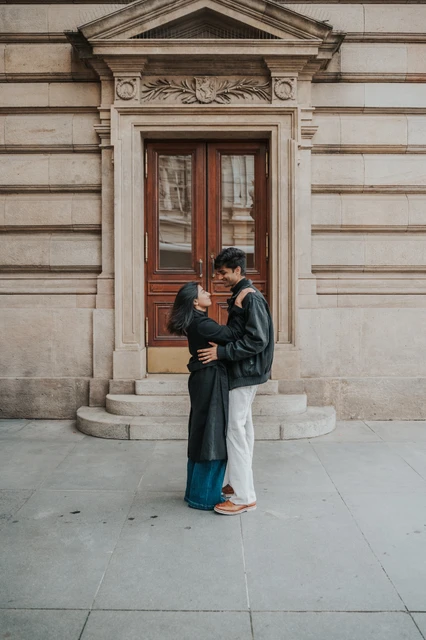 Prague couple photoshoot: an embrace framed by the theatre doorway Full-length portrait of the couple embracing beside an ornate theatre doorway during their Prague couple photoshoot.