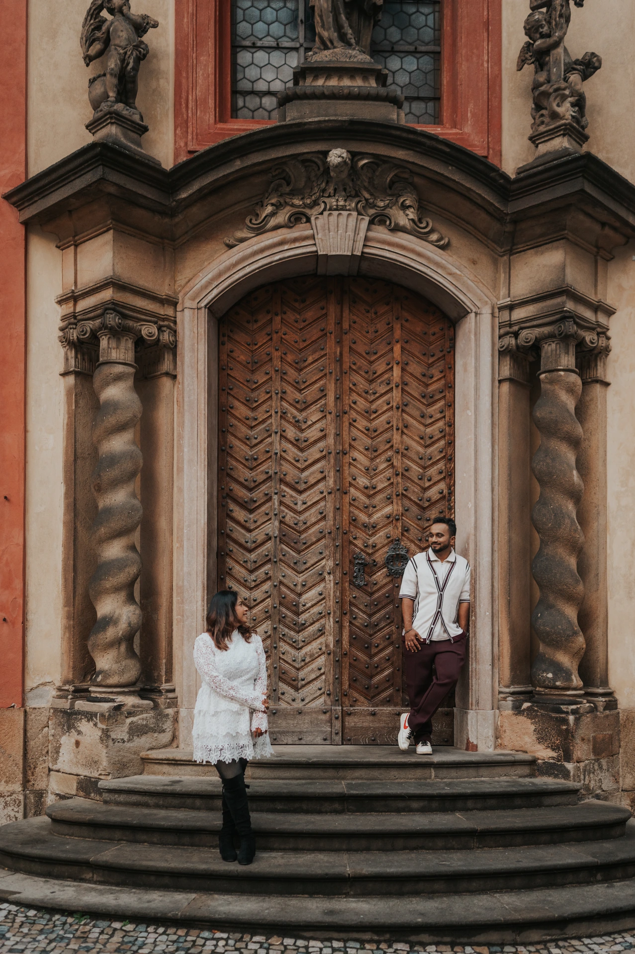 Couple standing apart on the steps of the ornate St. George's Basilica doorway during their couple photoshoot at Prague Castle.