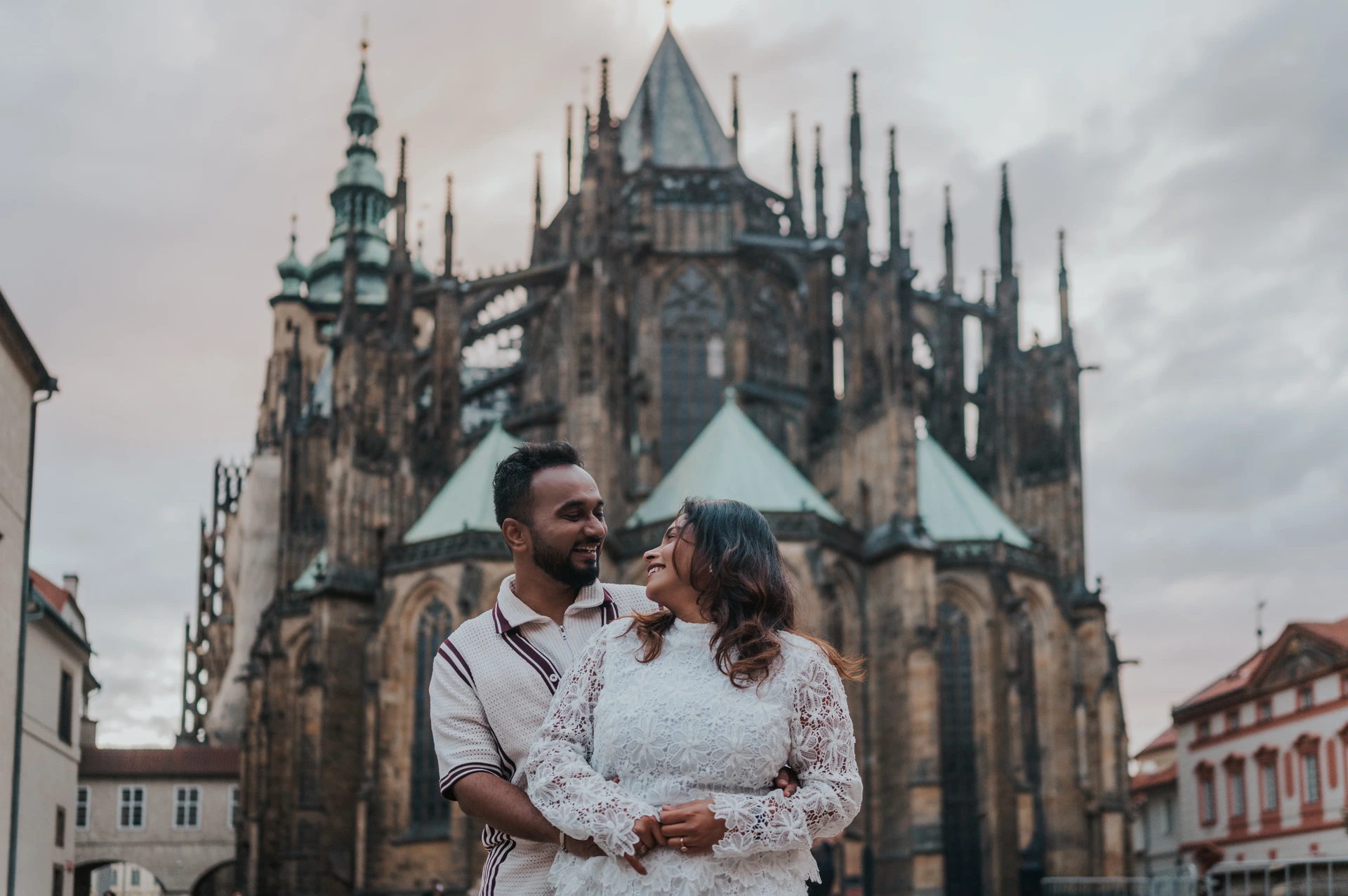 Prague couple photoshoot with St. Vitus Cathedral in the backdrop Landscape portrait of the couple smiling in an embrace with St. Vitus Cathedral in the backdrop during their Prague photoshoot.