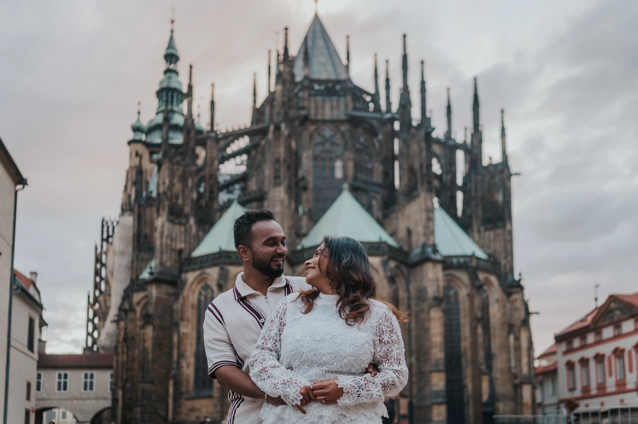 Prague couple photoshoot with St. Vitus Cathedral in the backdrop Landscape portrait of the couple smiling in an embrace with St. Vitus Cathedral in the backdrop during their Prague photoshoot.