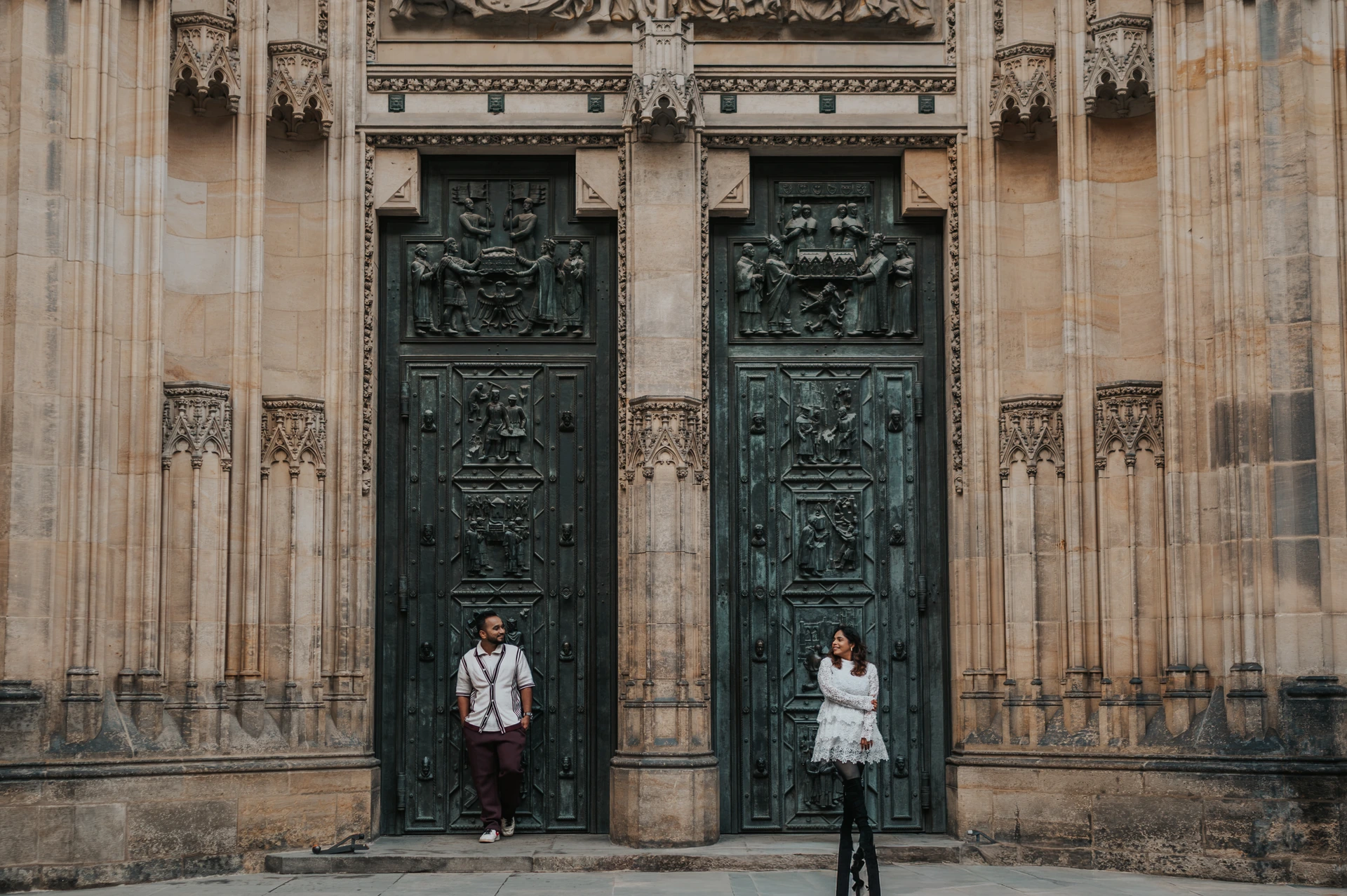 Wide Prague couple photoshoot by the cathedral doors Wide photograph of the couple standing beside the decorated St. Vitus Cathedral doors during their Prague couple photoshoot.