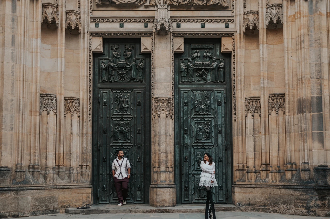 Wide Prague couple photoshoot by the cathedral doors Wide photograph of the couple standing beside the decorated St. Vitus Cathedral doors during their Prague couple photoshoot.