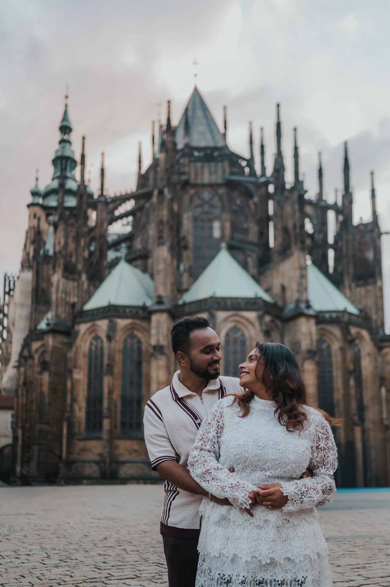 Couple embracing and smiling with St. Vitus Cathedral rising behind them during their couple photoshoot in Prague.