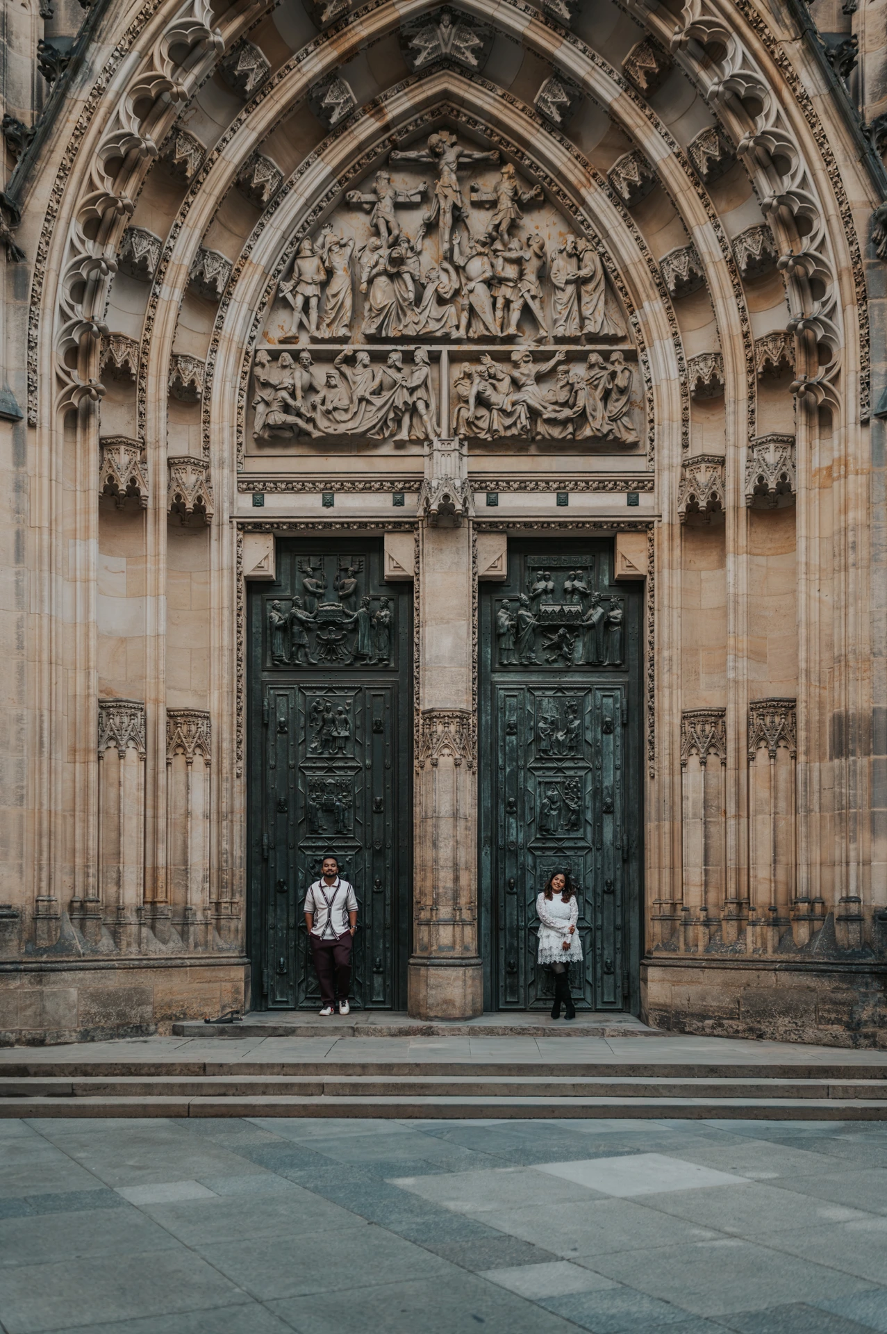 Couple standing apart beneath the carved Gothic portal of St. Vitus Cathedral during their couple photoshoot in Prague.