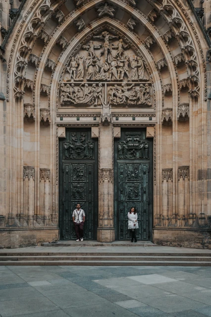 Couple standing apart beneath the carved Gothic portal of St. Vitus Cathedral during their couple photoshoot in Prague.