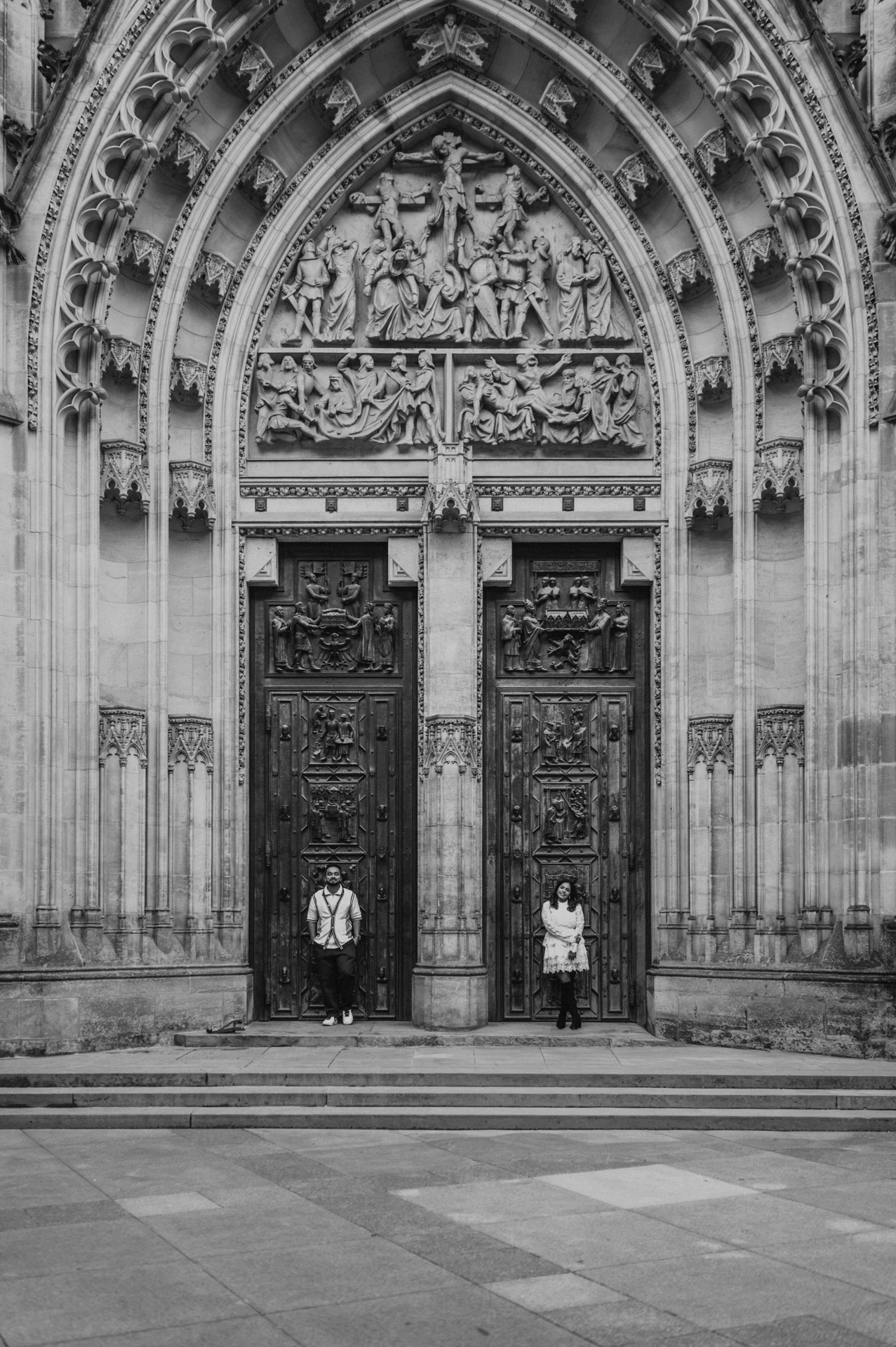 Black-and-white photograph of the couple beneath the tall St. Vitus Cathedral entrance during their Prague photoshoot.