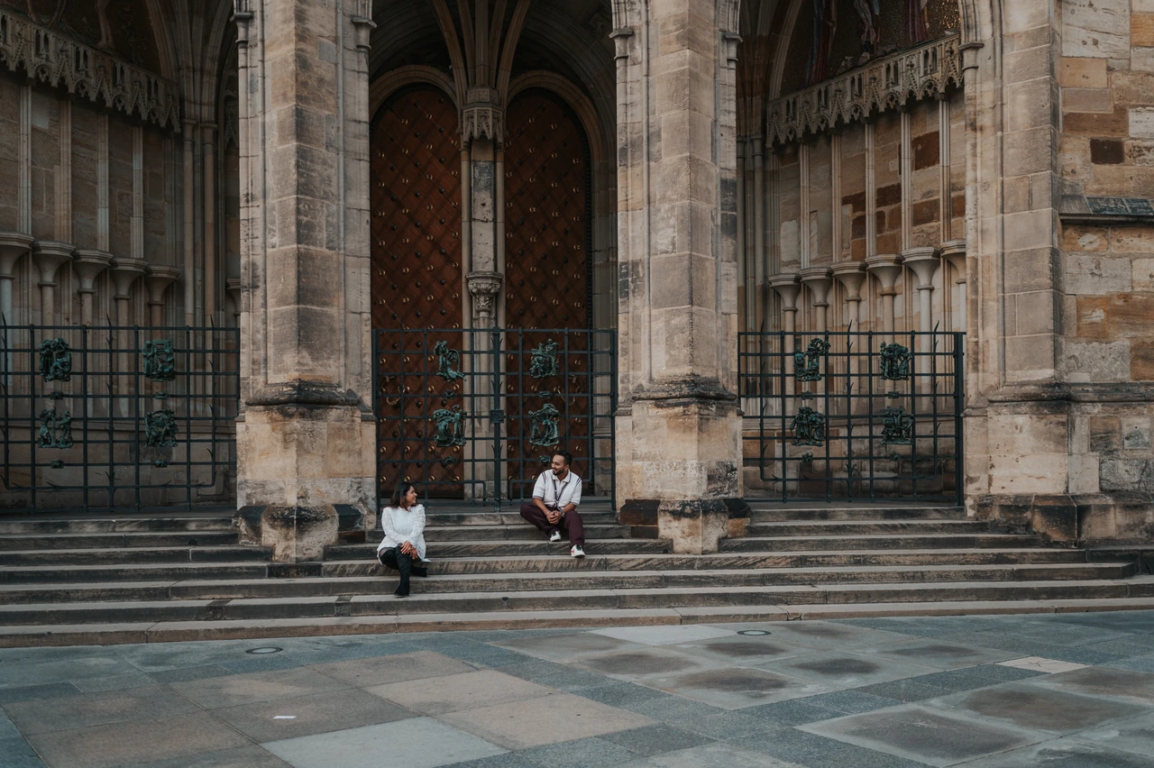 Prague couple photoshoot sitting on the cathedral steps Landscape photograph of the couple sitting on the broad steps below St. Vitus Cathedral during their Prague photoshoot.